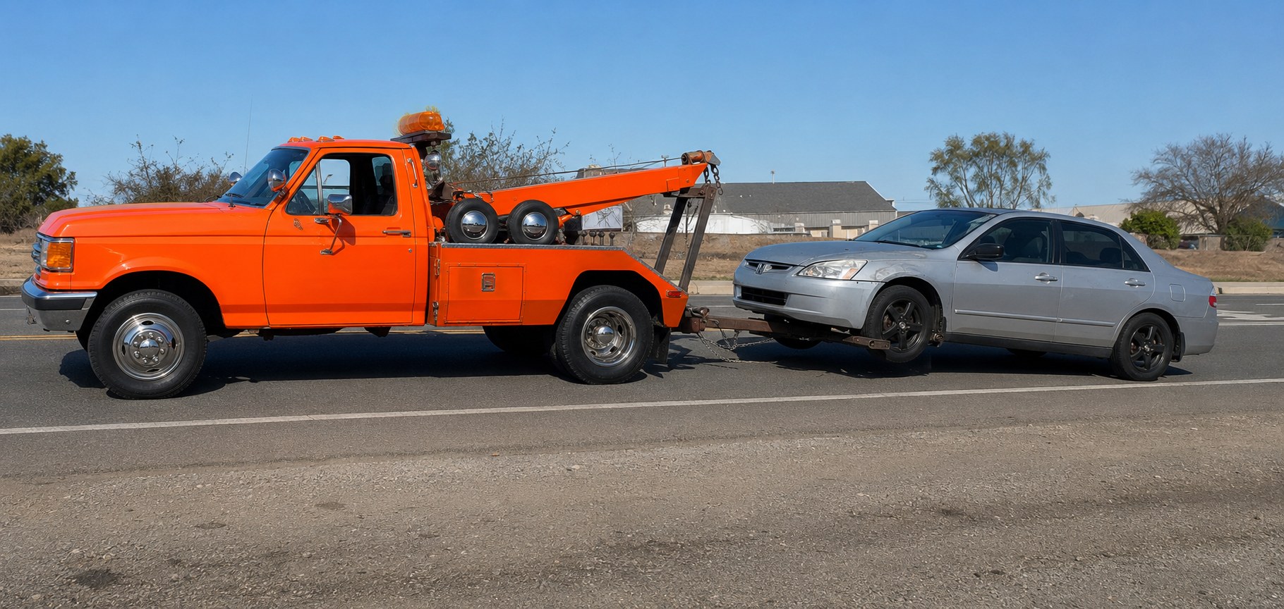 A tow truck towing a non-running sedan down a local road